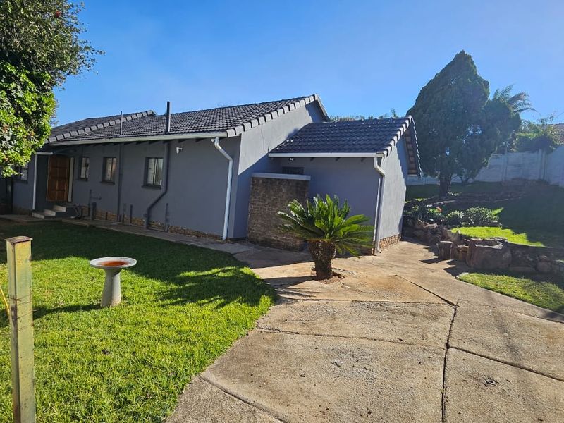 Rear view of the property featuring a concrete driveway, landscaped garden area, and a tiled roof structure with boundary walling.