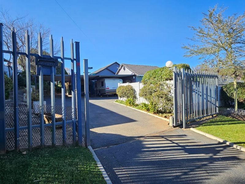 Front view of the property featuring a secure gated entrance, paved driveway, and a covered carport area.
