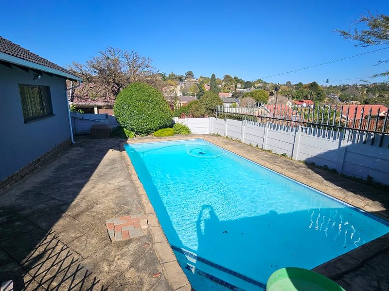Outdoor pool area featuring a rectangular swimming pool, paved surround, and secure perimeter walling with metal spikes.