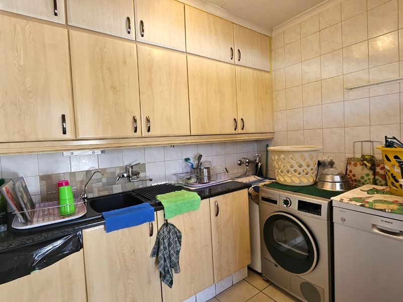 Functional laundry area featuring built-in cabinetry, laminate countertops, a sink, and tiled splashback, providing practical utility space with integrated appliance connections.