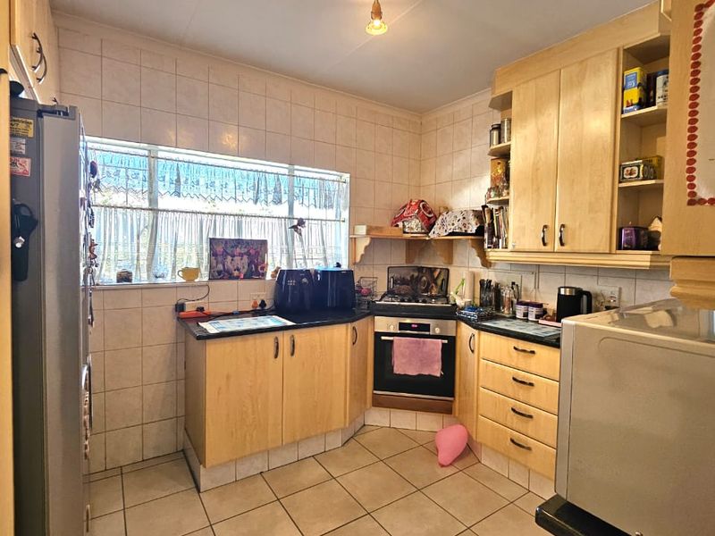 A functional kitchen featuring light wood cabinetry, tiled backsplash, and tiled flooring, equipped with a built-in oven and hob.