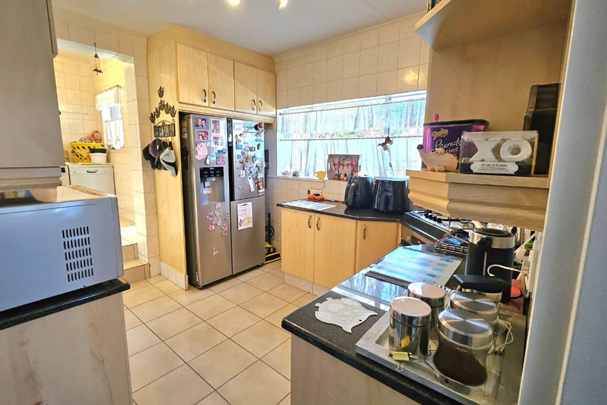Functional kitchen featuring light wood cabinetry, granite countertops, tiled flooring, and a tiled backsplash, with an adjacent scullery area visible.