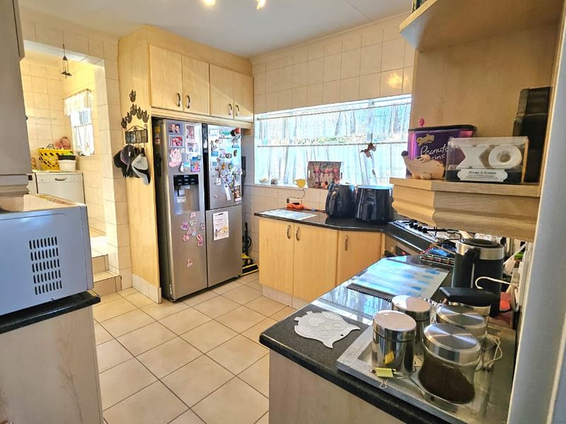Functional kitchen featuring light wood cabinetry, granite countertops, tiled flooring, and a tiled backsplash, with an adjacent scullery area visible.