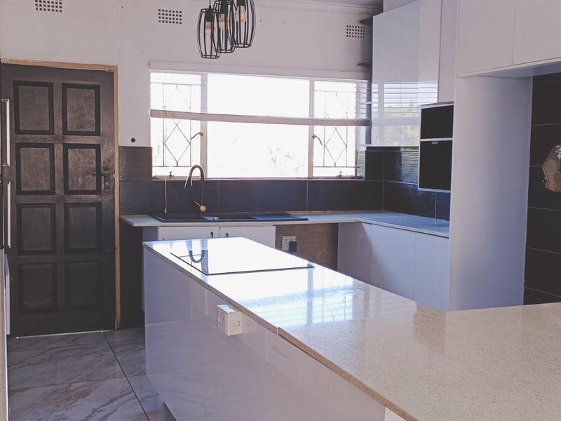 Modern kitchen featuring white cabinetry, stone countertops, a central island with a gas hob, and dark tiled backsplash, offering a clean, functional workspace.