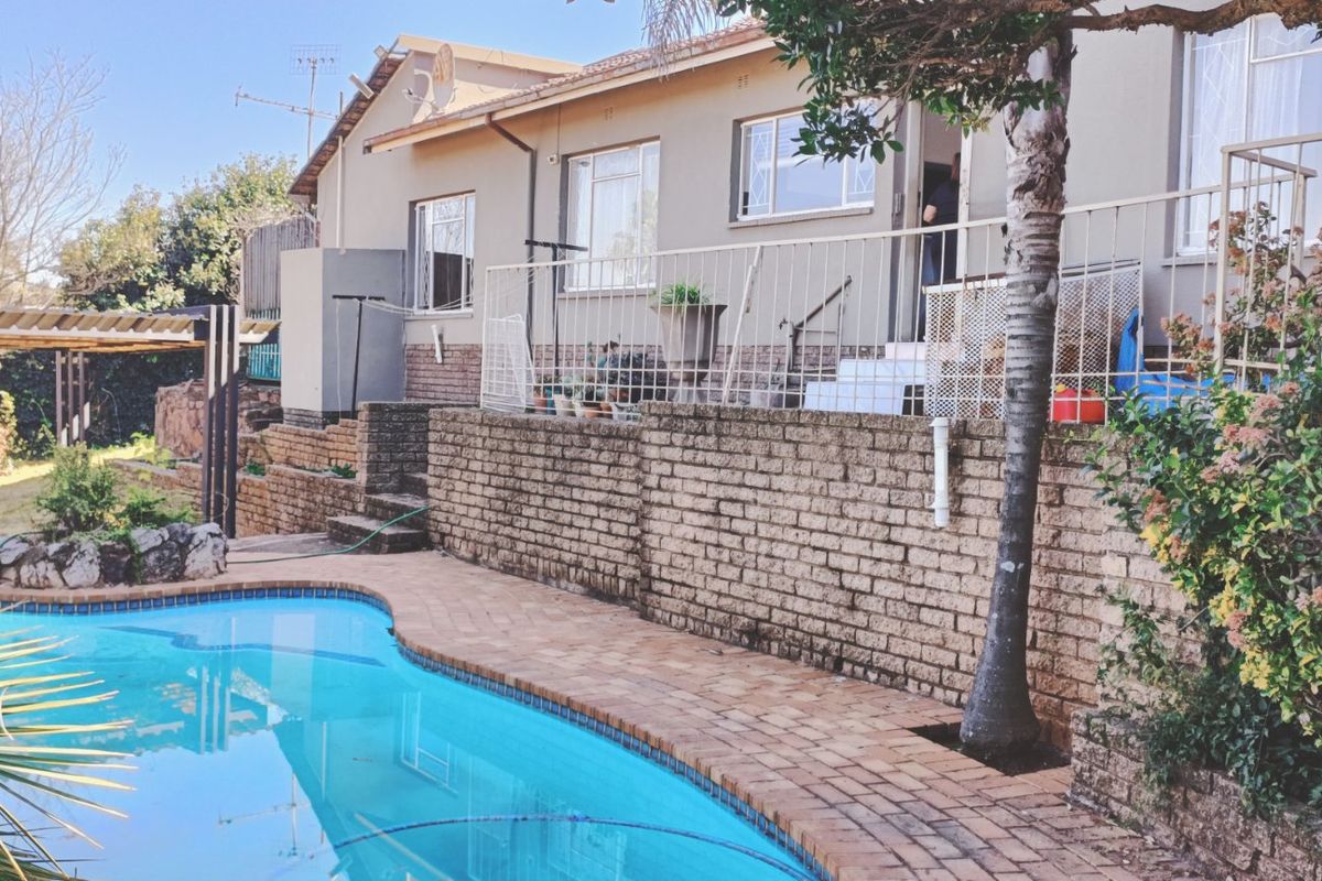 Rear exterior view featuring a swimming pool, paved surround, brick retaining wall, and a pergola structure.