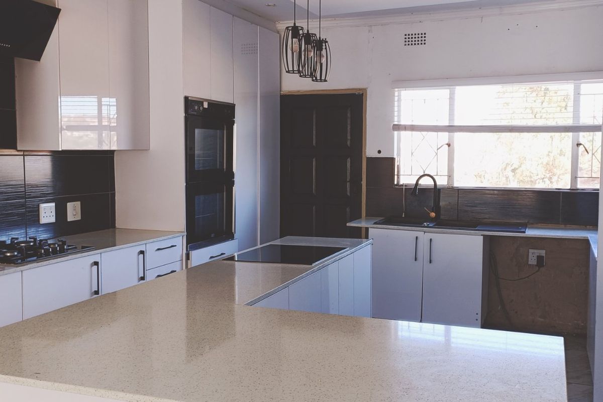 Modern kitchen featuring stone countertops, built-in oven, gas hob, and a central island. The space requires minor finishing touches to complete the cabinetry and walls.