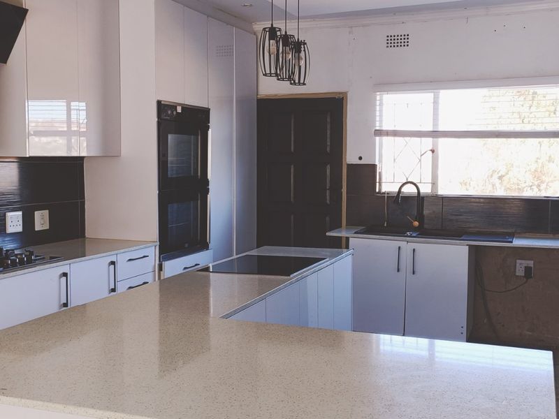 Modern kitchen featuring stone countertops, built-in oven, gas hob, and a central island. The space requires minor finishing touches to complete the cabinetry and walls.