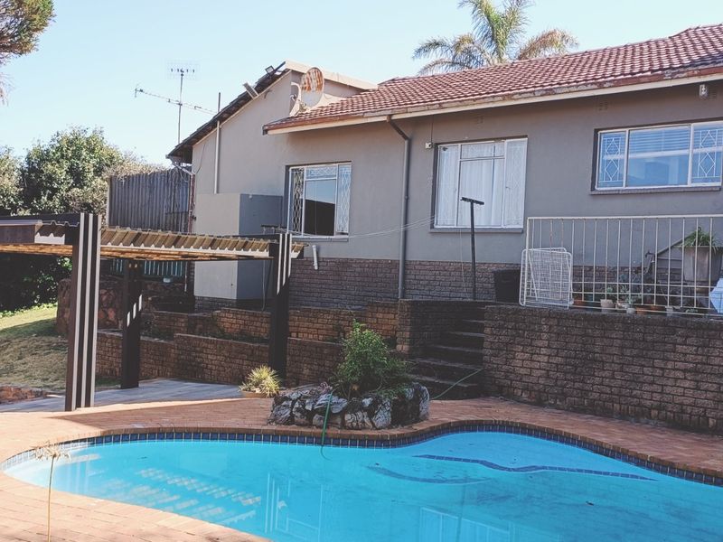 Rear exterior view featuring a swimming pool, brick retaining walls, a pergola, and direct access to the house via a raised patio.