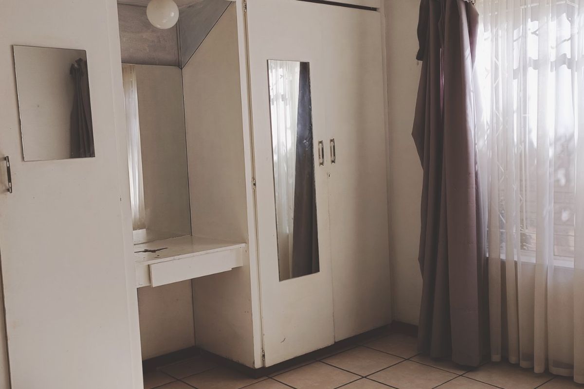 A bedroom featuring built-in cupboards and a vanity unit, with tiled flooring and natural light from a window with security bars.