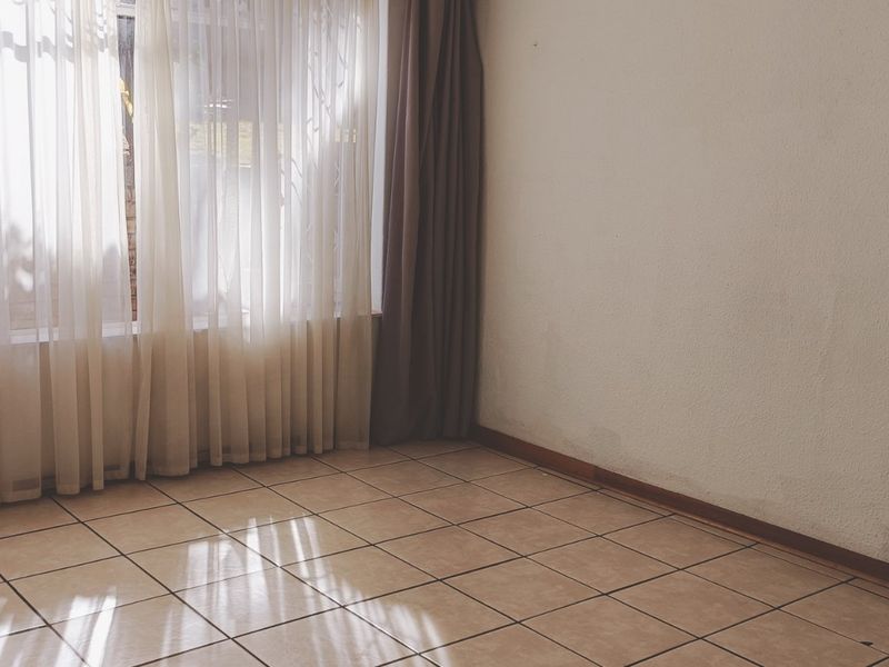An empty living room featuring tiled flooring, neutral walls, and large windows with curtains, offering a blank canvas for interior design.