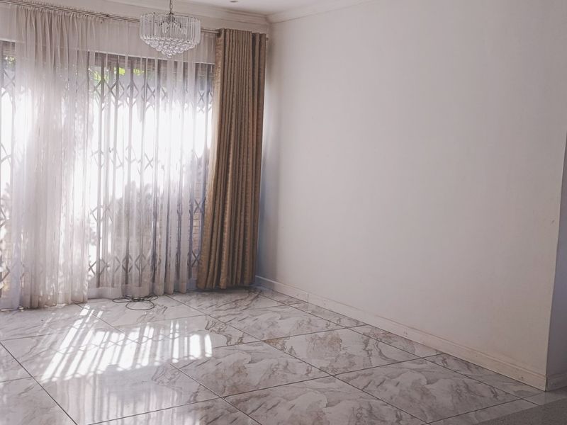 A bright, empty living room featuring large-format marble-look floor tiles, a crystal chandelier, and a sliding glass door with an integrated security gate.