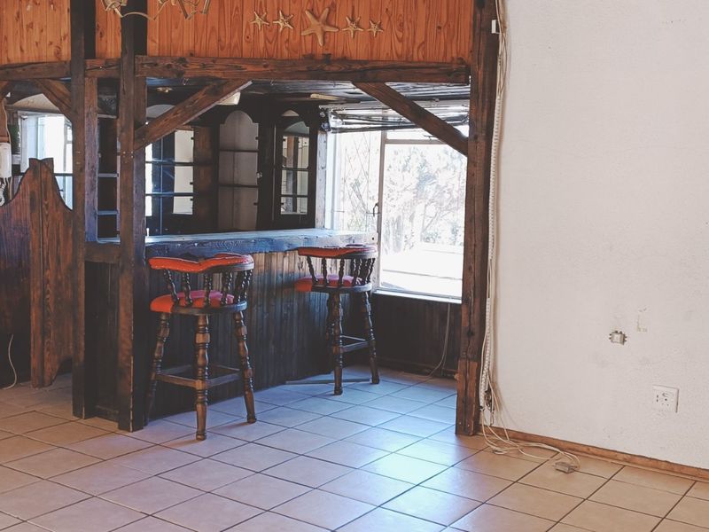 A dedicated bar area featuring a built-in timber counter and cabinetry, set against tiled flooring with an arched entryway.