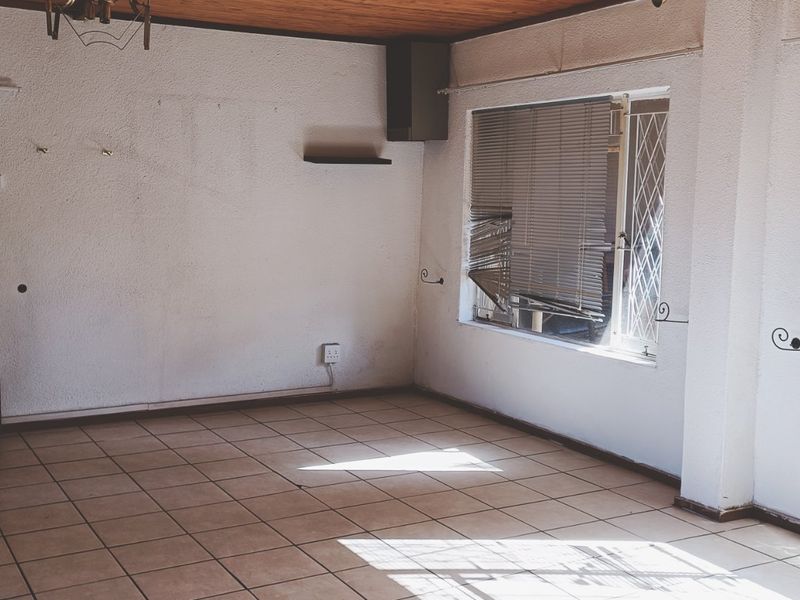 An empty living room featuring tiled flooring, a timber ceiling, and wall-mounted air conditioning, requiring cosmetic updates to improve its overall condition.