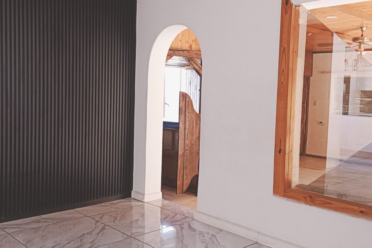 A bright living area featuring modern slatted wall paneling, polished tiled floors, and an arched doorway leading to an adjacent space.