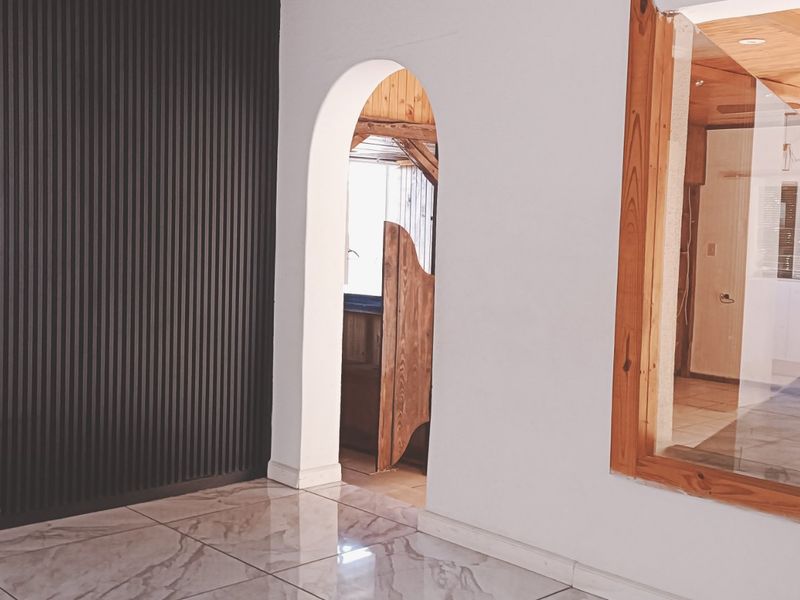 A bright living area featuring modern slatted wall paneling, polished tiled floors, and an arched doorway leading to an adjacent space.