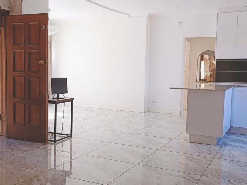 Open-plan living area featuring modern marble-look tiled flooring and a compact kitchen with white cabinetry and a central island.