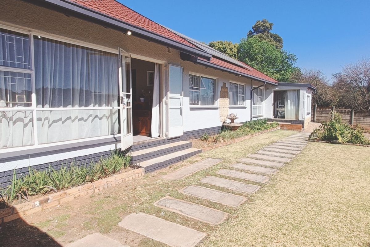 Rear view of the house featuring a tiled roof, concrete pathway, and a spacious garden area with a brick boundary wall.