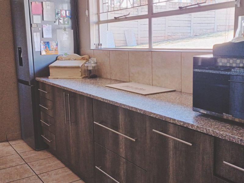 A functional kitchen featuring dark wood-look cabinetry, laminate countertops, a tiled backsplash, and tiled flooring with natural light from the window.