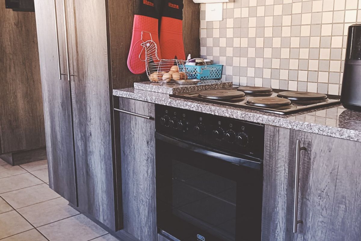 A functional kitchen featuring dark wood-grain cabinetry, granite countertops, a built-in electric oven and hob, and a mosaic tile backsplash.