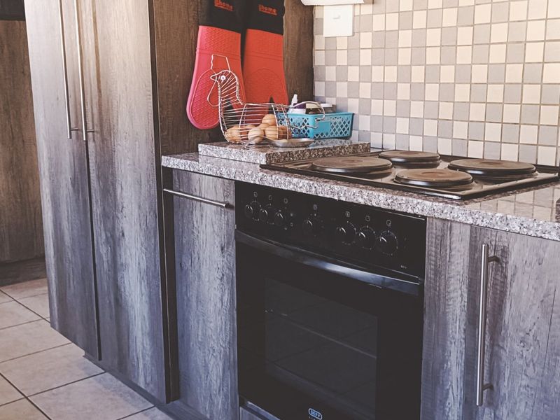 A functional kitchen featuring dark wood-grain cabinetry, granite countertops, a built-in electric oven and hob, and a mosaic tile backsplash.