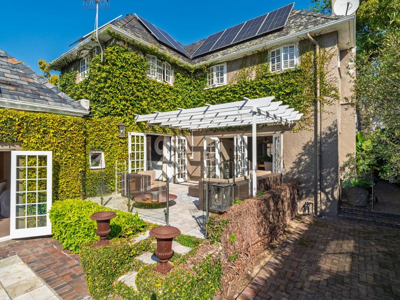 Rear exterior view featuring a paved patio area with a white pergola, glass balustrade, and climbing ivy on the building facade.