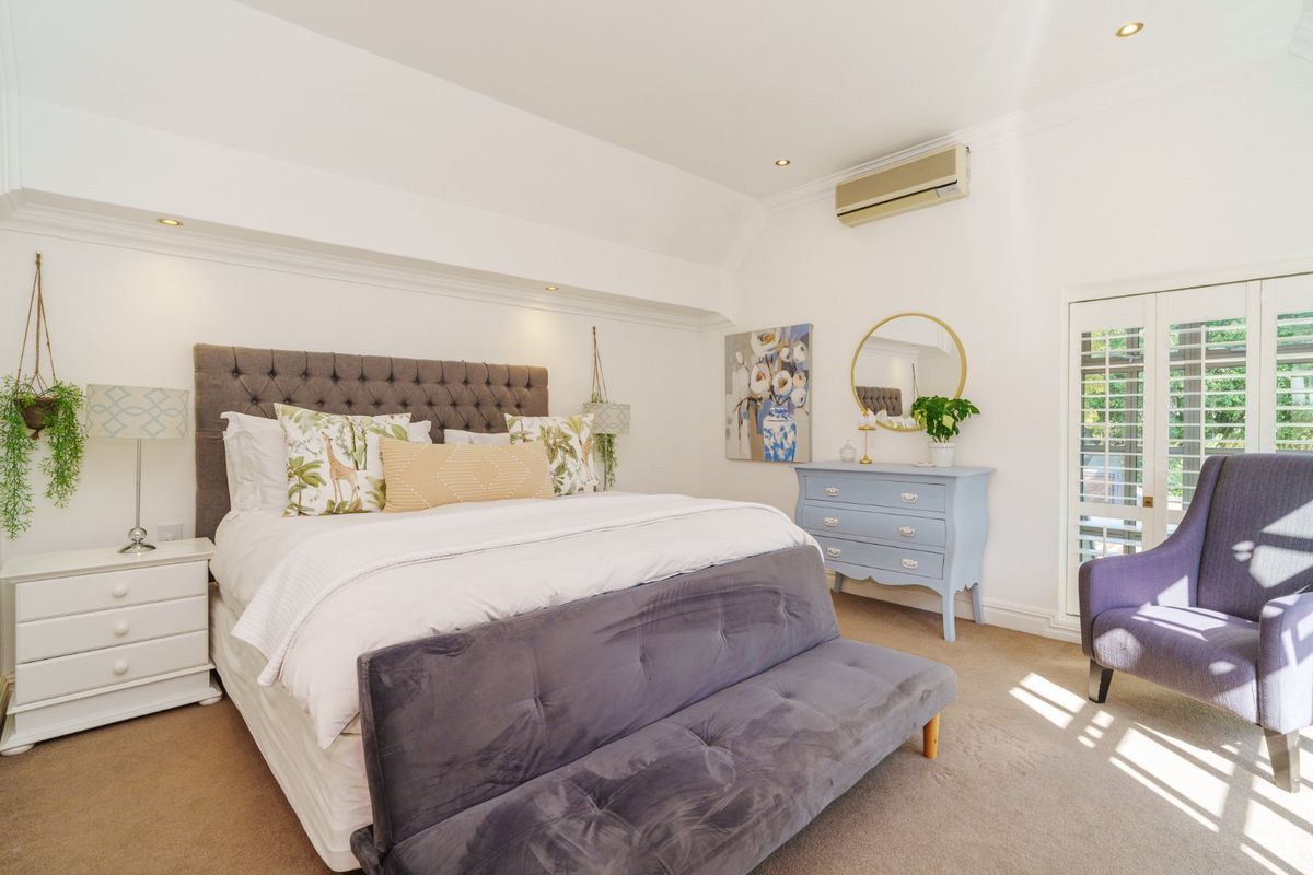 A well-maintained bedroom featuring carpeted flooring, recessed downlighting, a split-system air conditioner, and french doors with plantation shutters leading to the exterior.