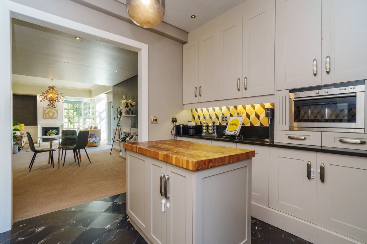 Modern kitchen featuring shaker-style cabinetry, a butcher block island, stone countertops, and a striking geometric tile backsplash, flowing into the adjacent living area.