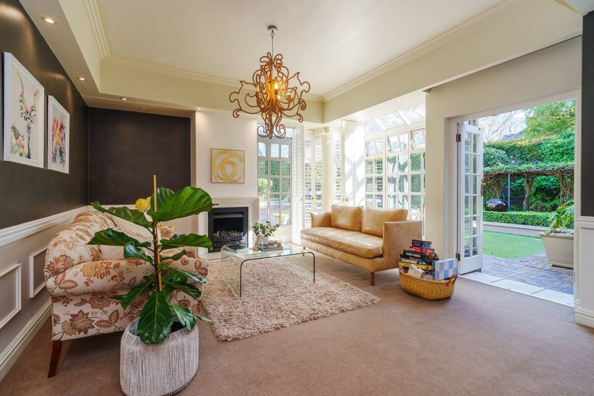 A bright and elegant living room featuring a fireplace, crown molding, and double french doors opening onto a private garden patio.