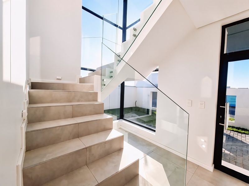 Modern entrance hallway featuring a tiled staircase with a sleek glass balustrade and expansive floor-to-ceiling windows providing abundant natural light.