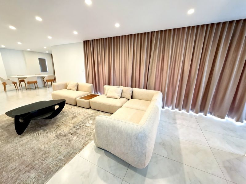Spacious open-plan living area featuring modern porcelain floor tiles, recessed downlighting, and floor-to-ceiling curtains creating a bright and contemporary atmosphere.