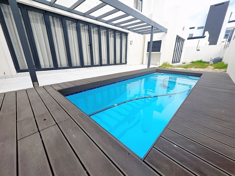 Modern outdoor entertainment area featuring a swimming pool with timber decking, a tiled patio, and a pergola, perfect for relaxed outdoor living.