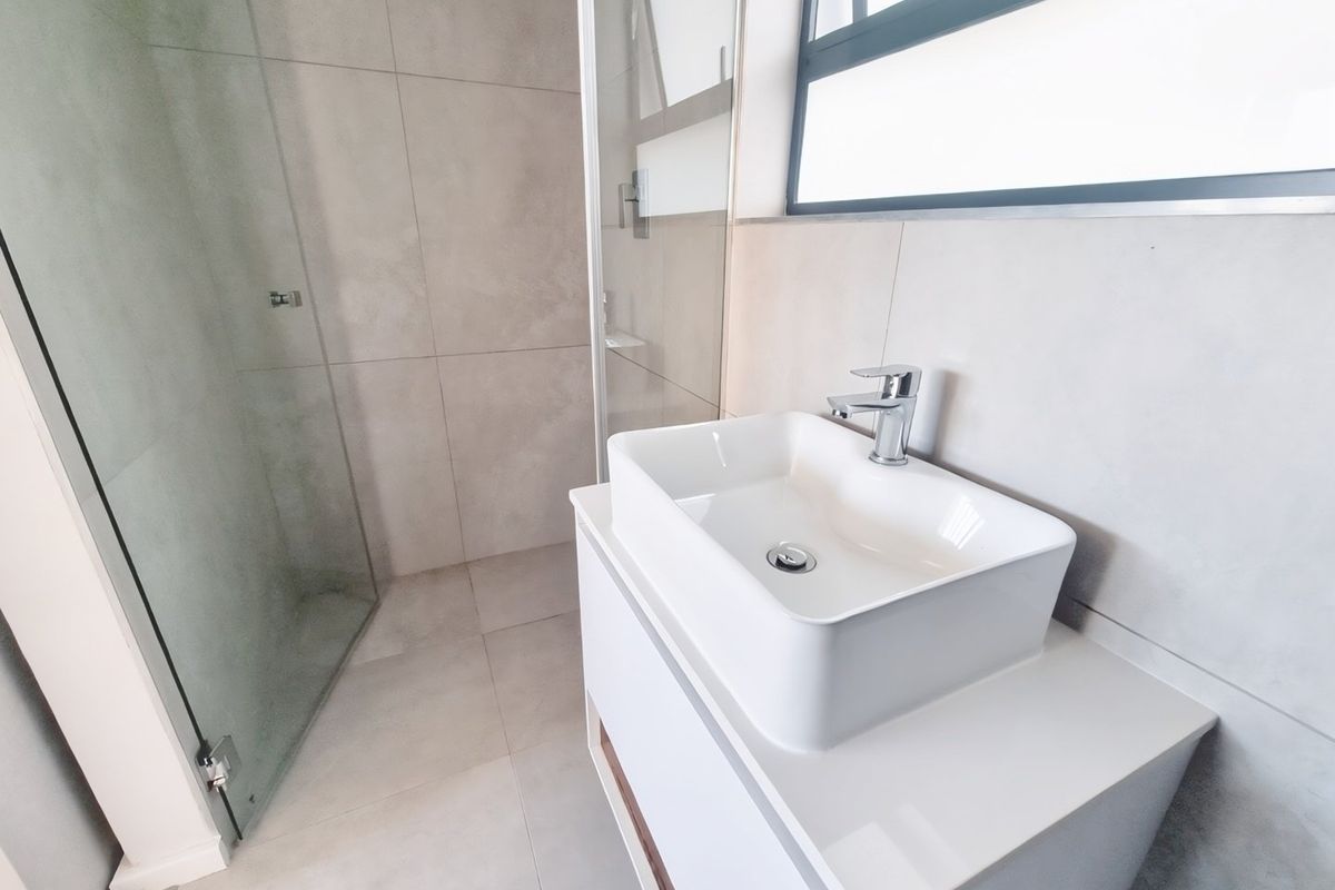 Modern bathroom featuring a sleek vessel sink on a vanity cabinet, large format neutral tiling, and a glass-enclosed shower.
