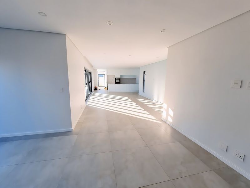 Spacious open-plan living and kitchen area featuring modern tiled flooring, recessed lighting, and clean white finishes, offering a bright and versatile living space.