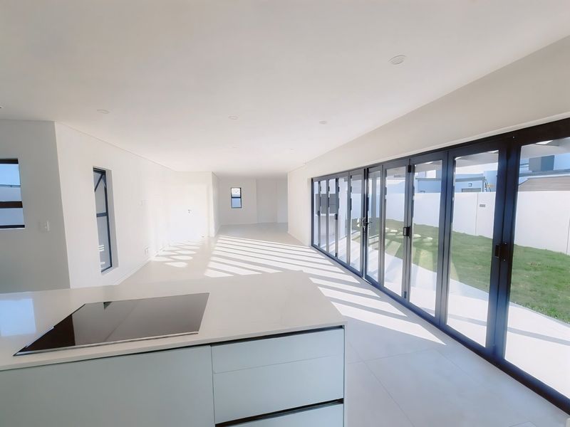 Spacious open-plan living area featuring a modern kitchen island with induction hob, sleek tiled floors, and large stacker doors opening to the garden.