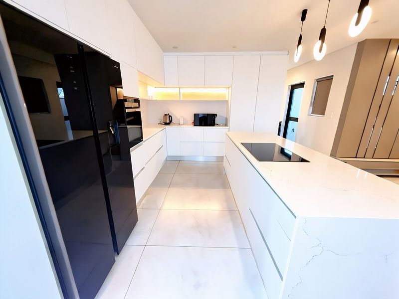 Modern kitchen featuring a large stone-topped island with integrated induction cooktop, handleless white cabinetry, and sleek porcelain floor tiles.