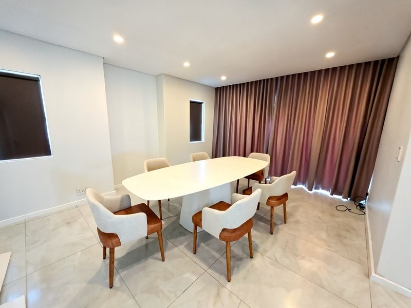 A modern dining room featuring large-format porcelain floor tiles, recessed ceiling lighting, and full-length window curtains.