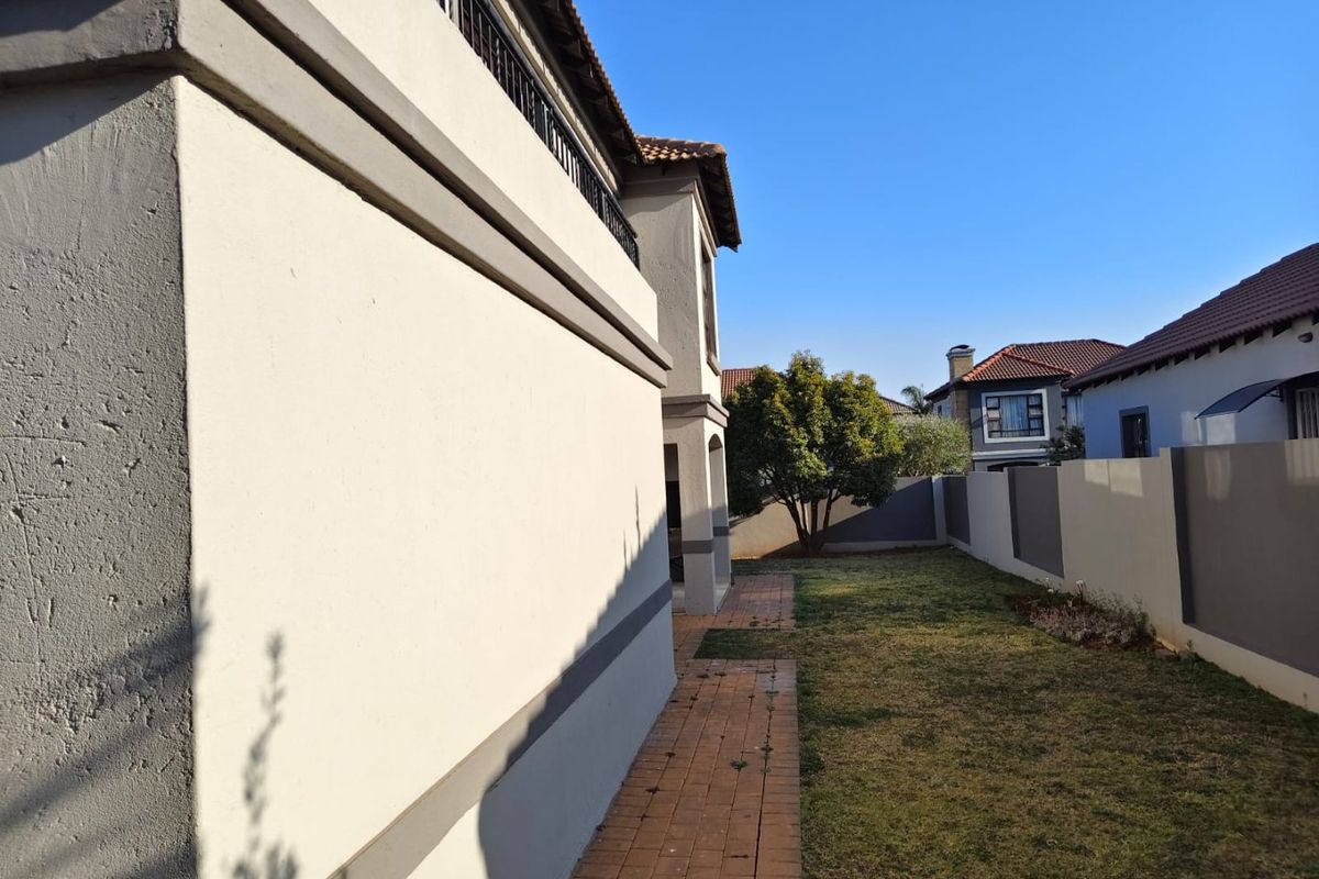 A view of the rear exterior of the property featuring a paved walkway, a well-maintained lawn, and perimeter boundary walls.