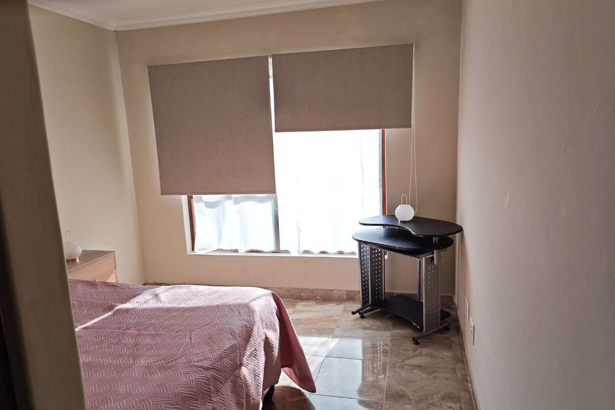 A bedroom featuring tiled flooring, neutral wall tones, and roller blinds, providing a functional and well-lit living space.