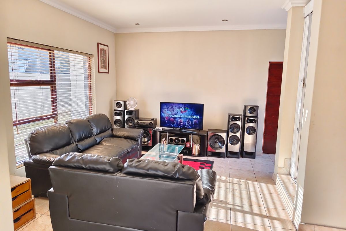 A comfortable living room featuring tiled flooring, recessed downlighting, and large windows fitted with venetian blinds.