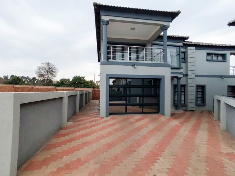 Front view of a modern two-story house featuring a paved driveway, secure garage, and an upper-level balcony with metal railings.