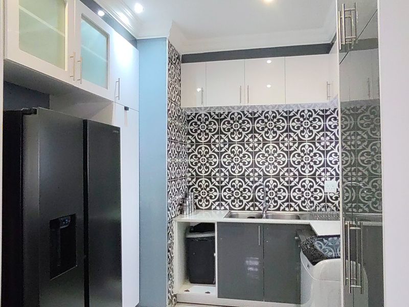 A modern scullery featuring high-gloss cabinetry, a stainless steel sink, and striking patterned tile splashbacks, providing a functional and stylish secondary prep area.