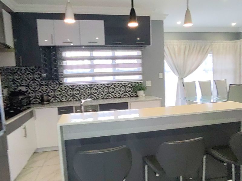 Modern open-plan kitchen featuring a breakfast island, patterned tile backsplash, and contemporary cabinetry, seamlessly flowing into the adjacent dining area.