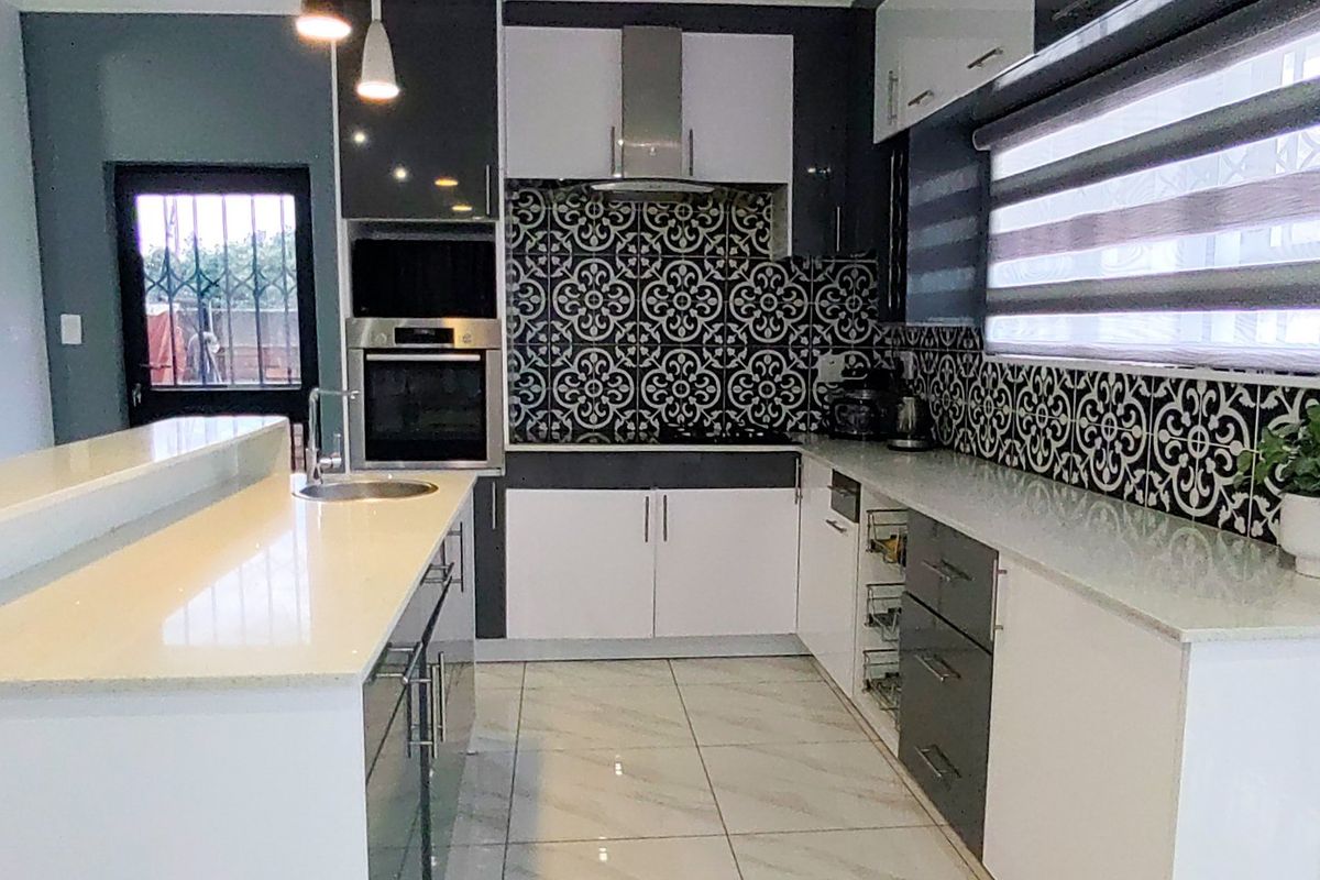 Modern kitchen featuring high-gloss cabinetry, stone countertops, a striking patterned tile backsplash, built-in oven, and sleek porcelain floor tiles.