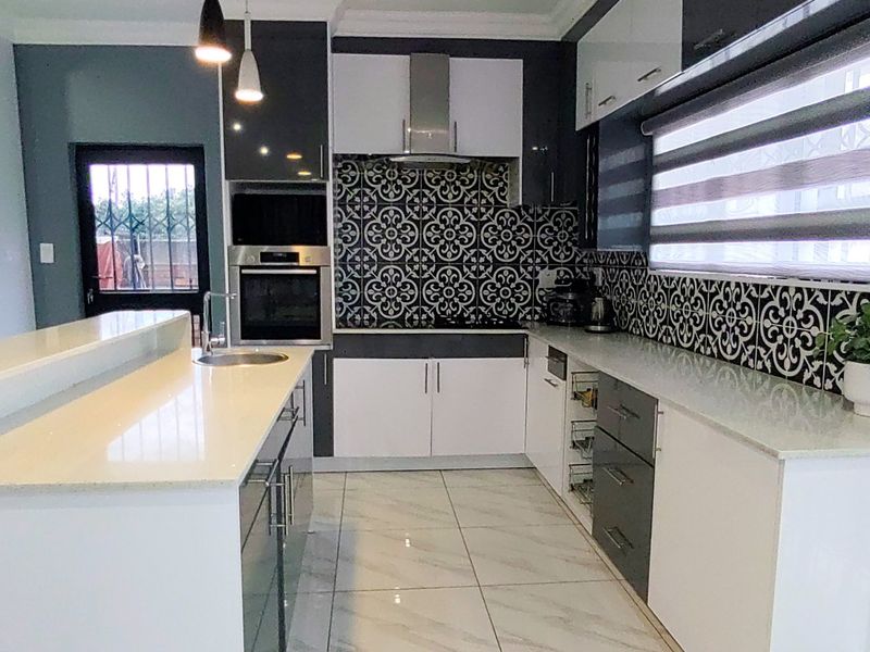 Modern kitchen featuring high-gloss cabinetry, stone countertops, a striking patterned tile backsplash, built-in oven, and sleek porcelain floor tiles.