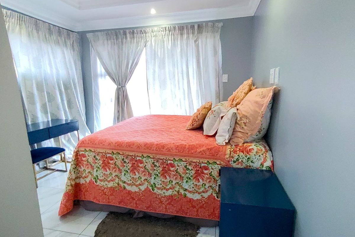 A well-lit bedroom featuring tiled flooring, a recessed ceiling with cove lighting, and large windows with curtains.