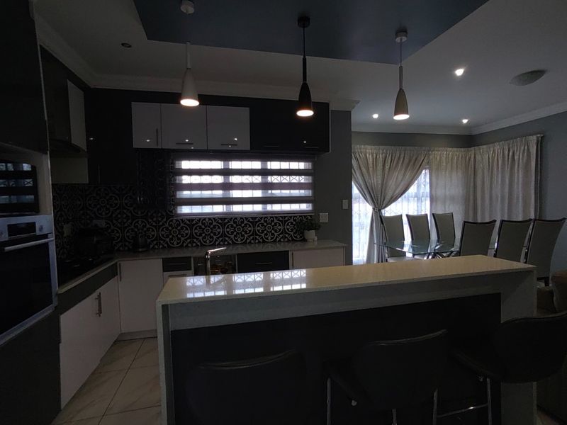 Modern open-plan kitchen featuring a breakfast island with quartz countertops, patterned backsplash, built-in oven, and stylish pendant lighting, seamlessly flowing into the dining area.
