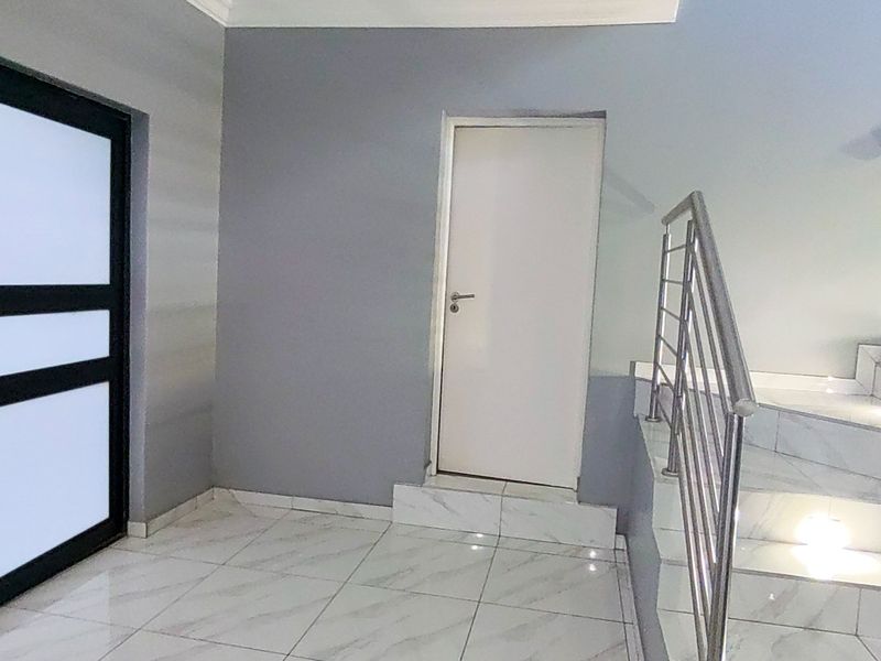 A bright, modern hallway featuring tiled flooring, a stainless steel balustrade, and a staircase leading to the upper level.