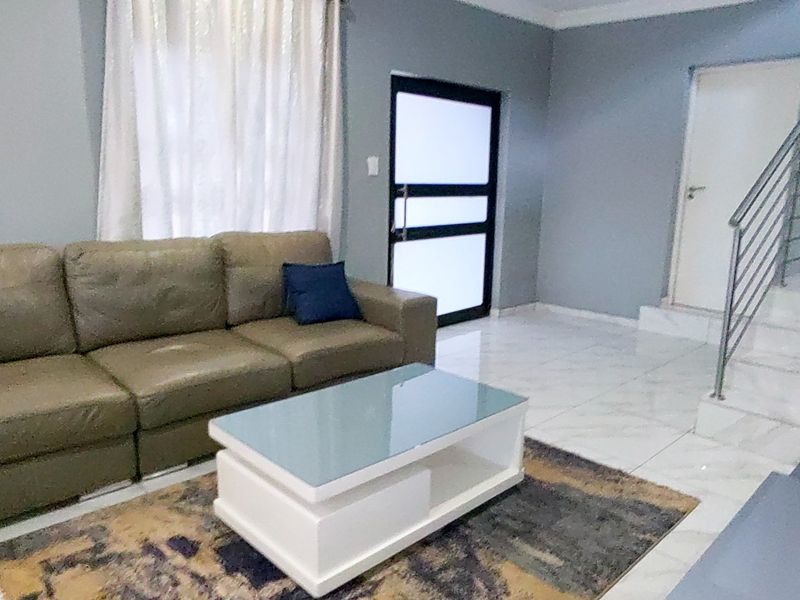 A living room featuring tiled flooring, a staircase with a metal railing, and a modern frosted glass panel door.