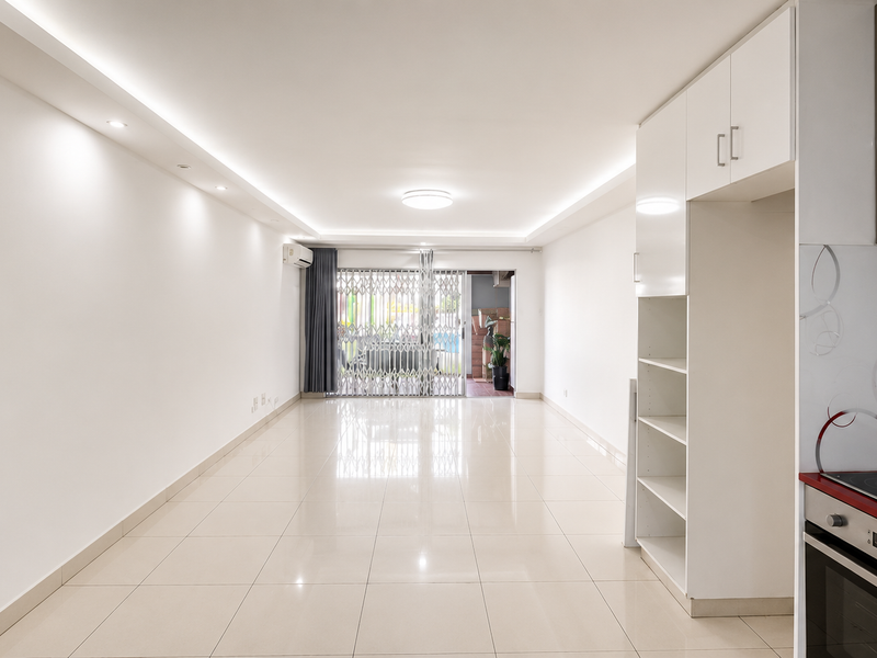 Spacious open-plan living area featuring tiled floors, recessed lighting, and a modern kitchen with built-in oven and hob, leading to a secure patio.
