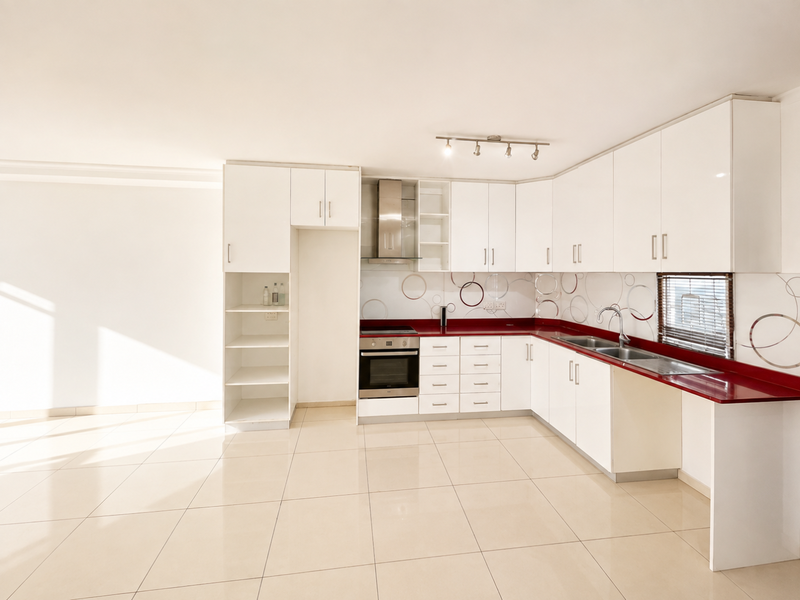 A clean, modern kitchen featuring white cabinetry, a striking red countertop, stainless steel appliances, and neutral tiled flooring in an open-plan layout.